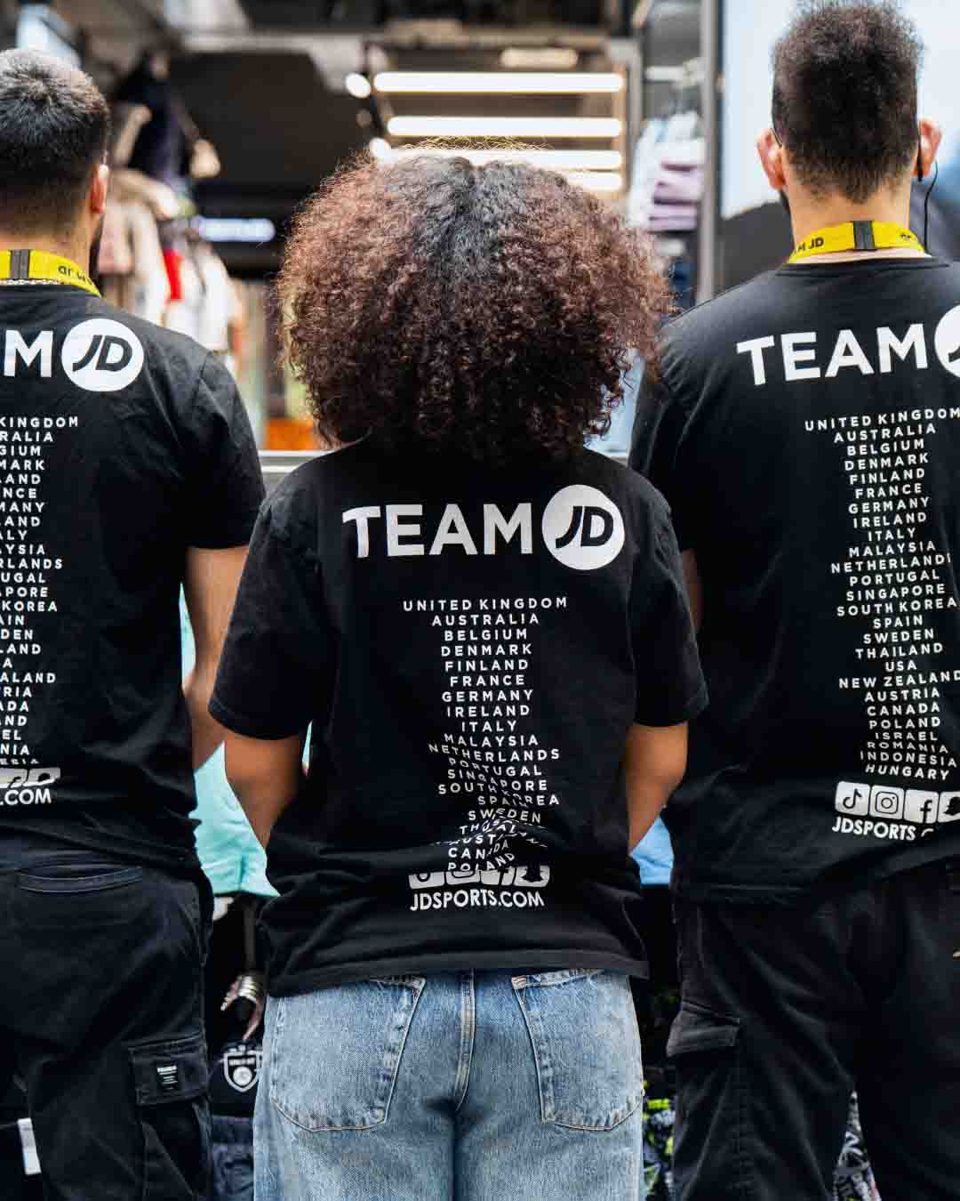 employés de JD Sports de dos, qui portent des t-shirts de jd sport